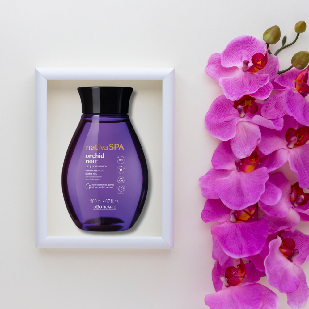 A bottle of purple body oil next to a vibrant purple orchid, showcasing O Boticário Nativa Spa Óleo Corporal Orquídea Noire.