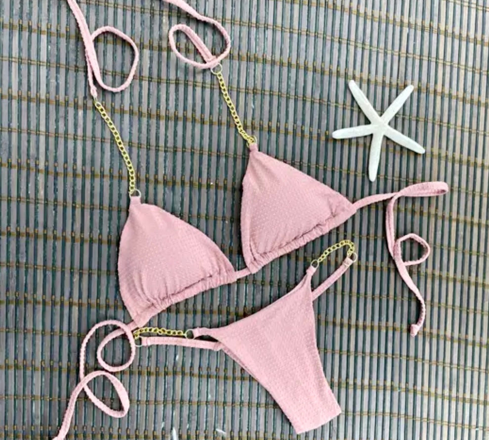 A pink bikini set with strap details in the form of chains, displayed on a wooden surface alongside a starfish.