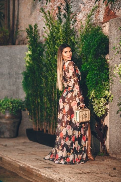 This image shows a person wearing a long-sleeved floral maxi dress. The dress features a busy, colorful floral print on a dark background and a high slit on the side.