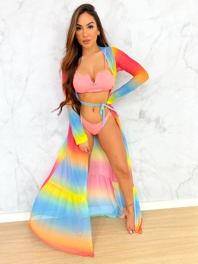 A model wearing a multicolored striped cover up with long sleeves and a tie at the waist, posing on a marble surface.