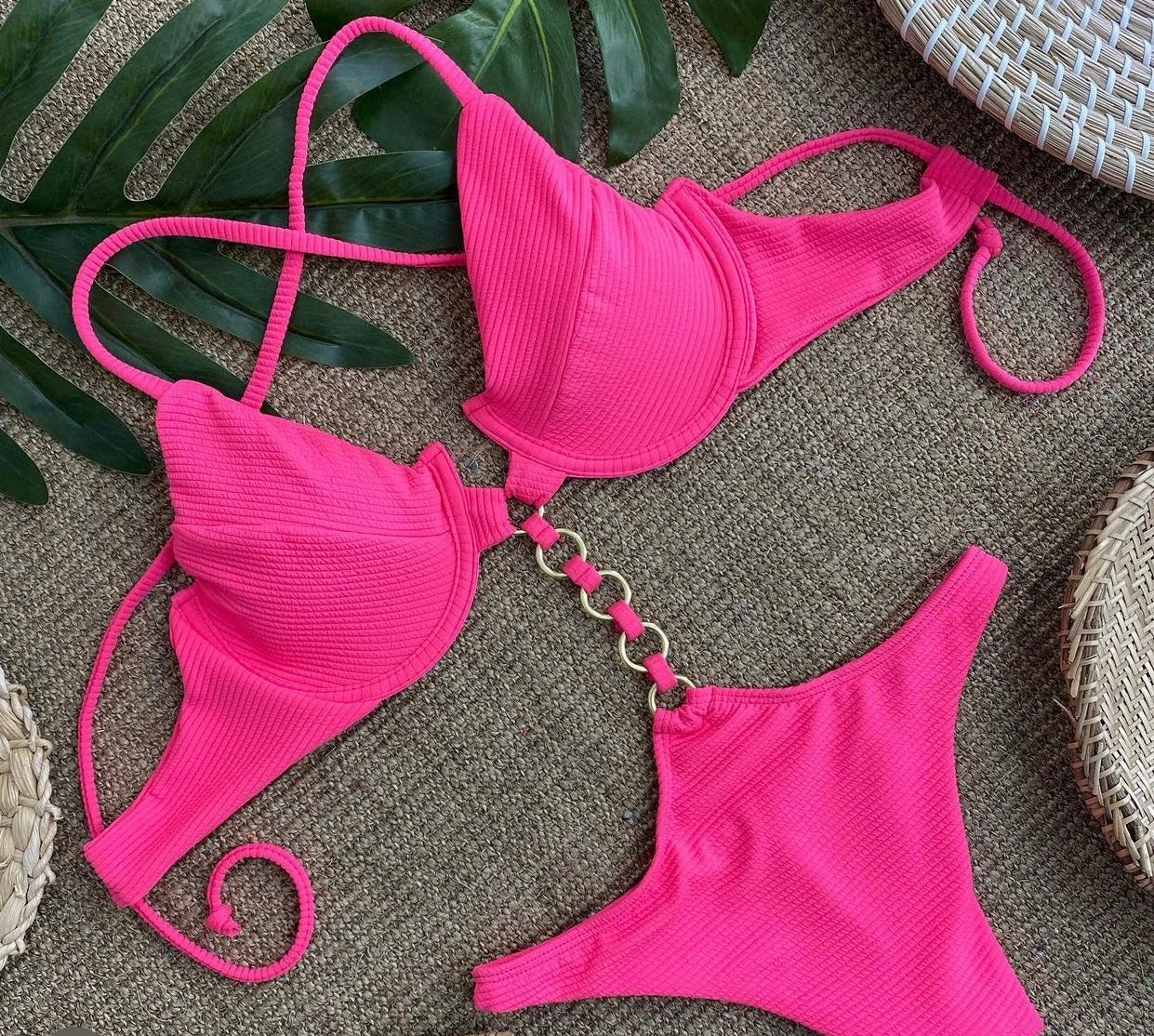 A pink two-piece swimsuit with textured fabric, displayed on a brown surface with a green leaf and a white and brown object in the background.