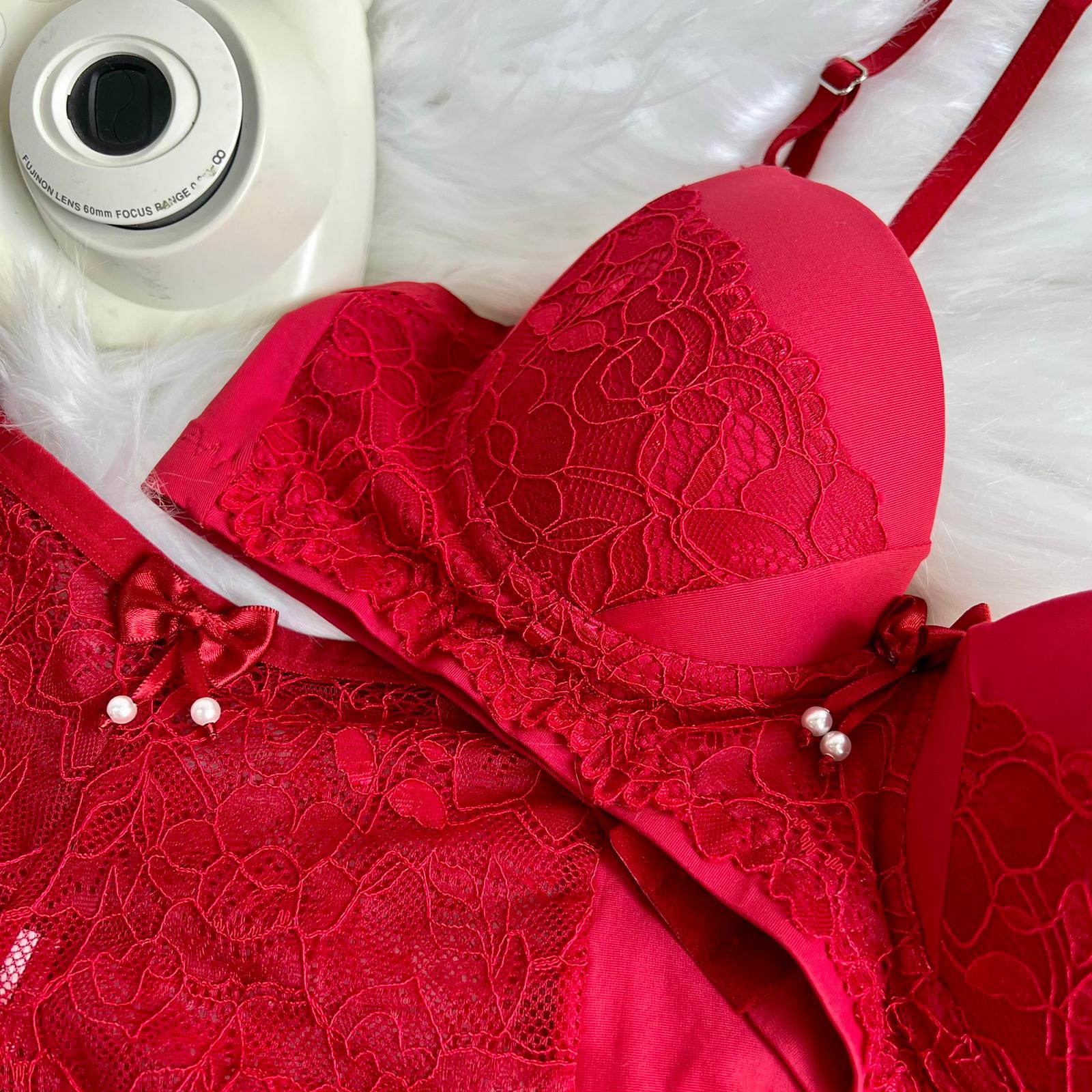 Red lace bra and panty set with bow details and metal adjustment straps on a white furry surface.